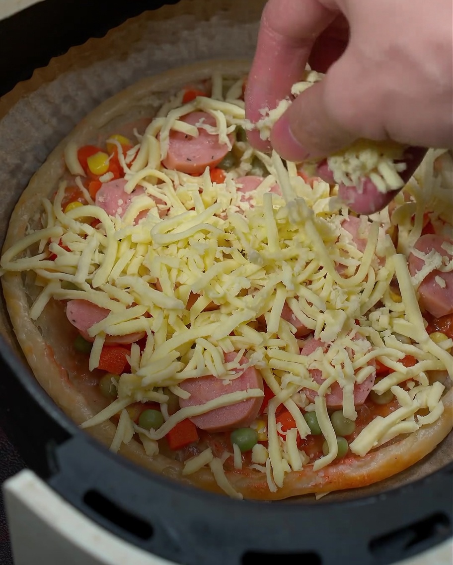 Eine Nahaufnahme von geriebenem Mozzarella-Käse, der über den Pizzazutaten verstreut wird.