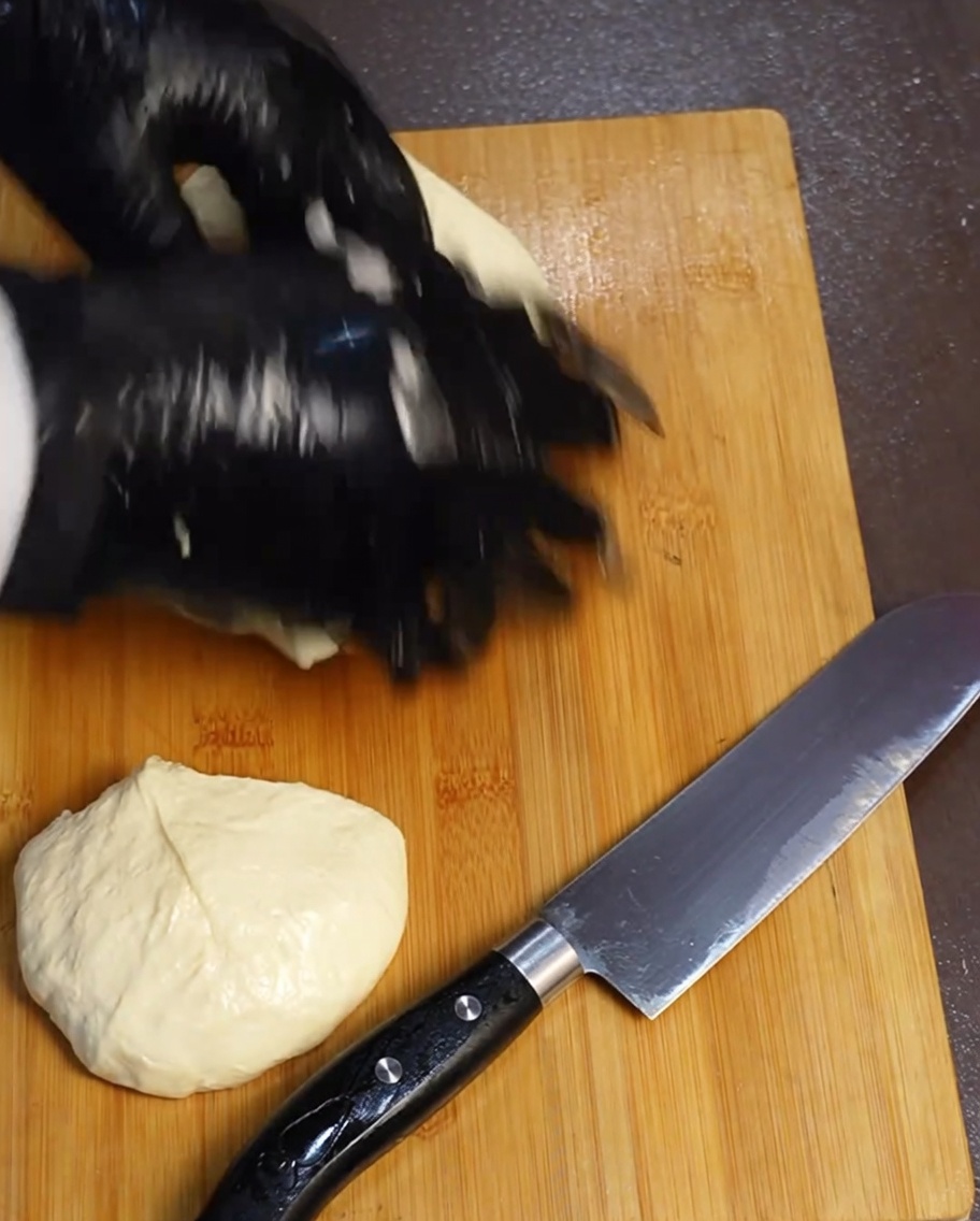 Vier gleiche Teigportionen auf einem Holzbrett neben einem Messer.