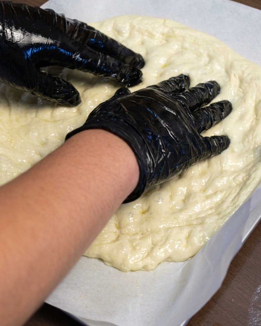 Hände dehnen den Pizzateig auf Backpapier nach außen.
