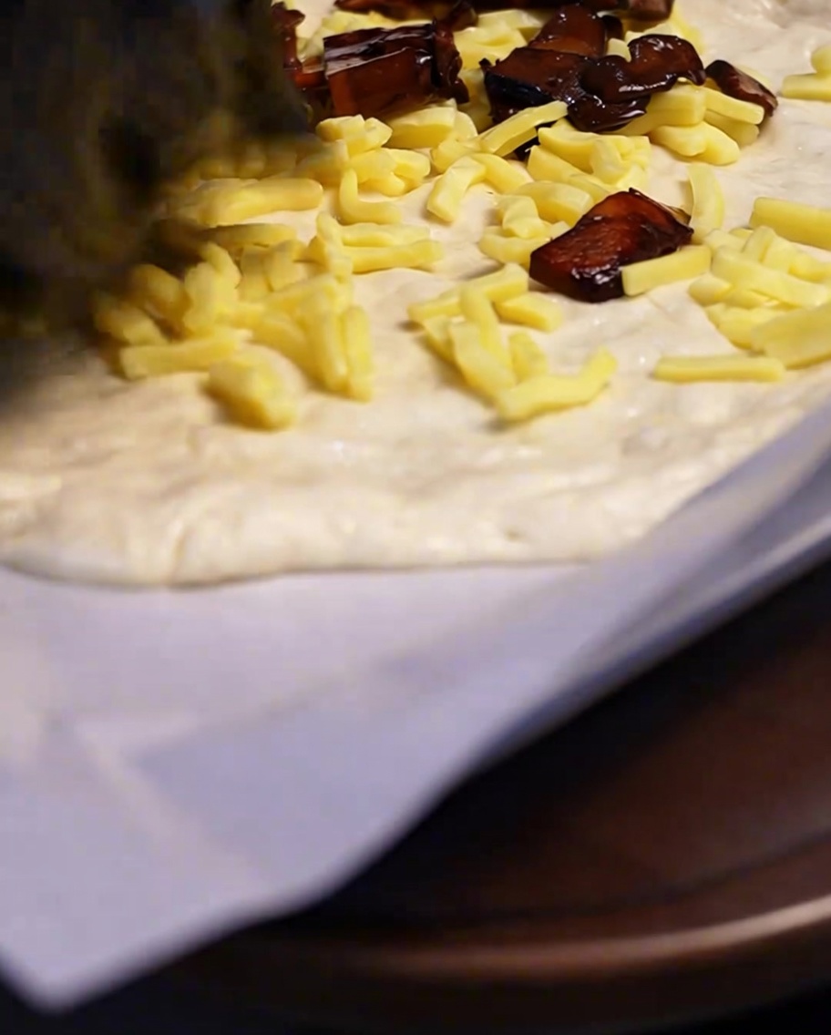 Gebratene, gewürzte Pilze werden auf eine Käseschicht auf dem Pizzaboden verteilt.