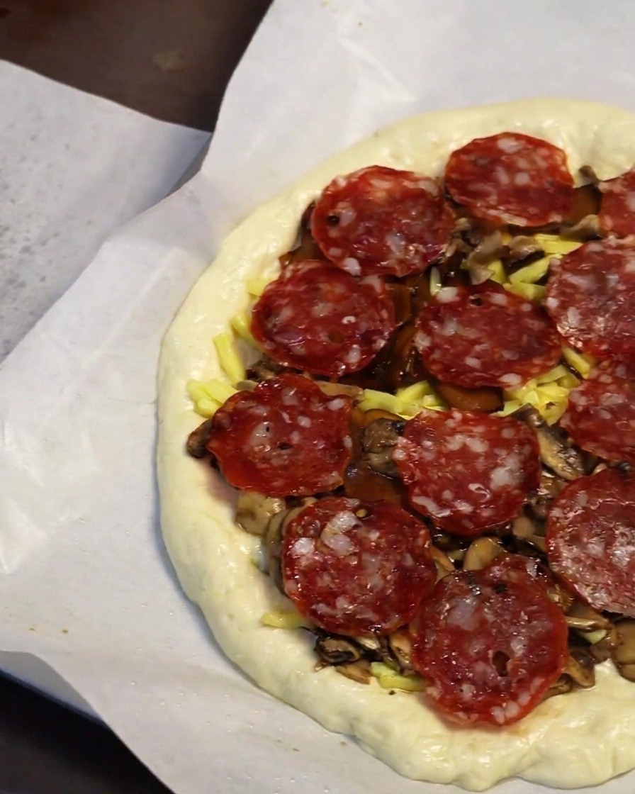 Nahaufnahme einer Hand, die Peperoni-Scheiben auf die Pizza legt.