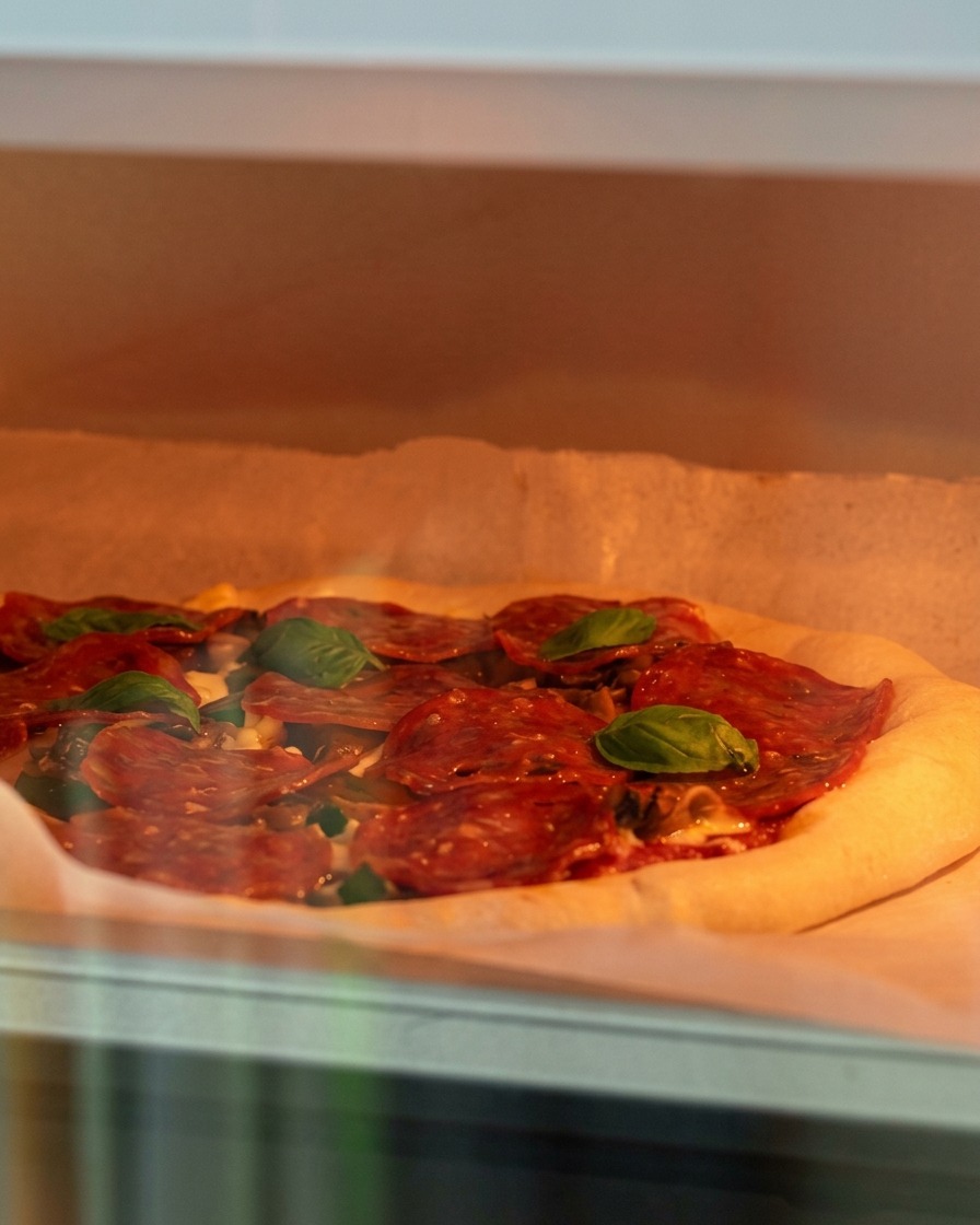 Eine belegte, rohe Pizza wird in einen heißen Ofen geschoben.