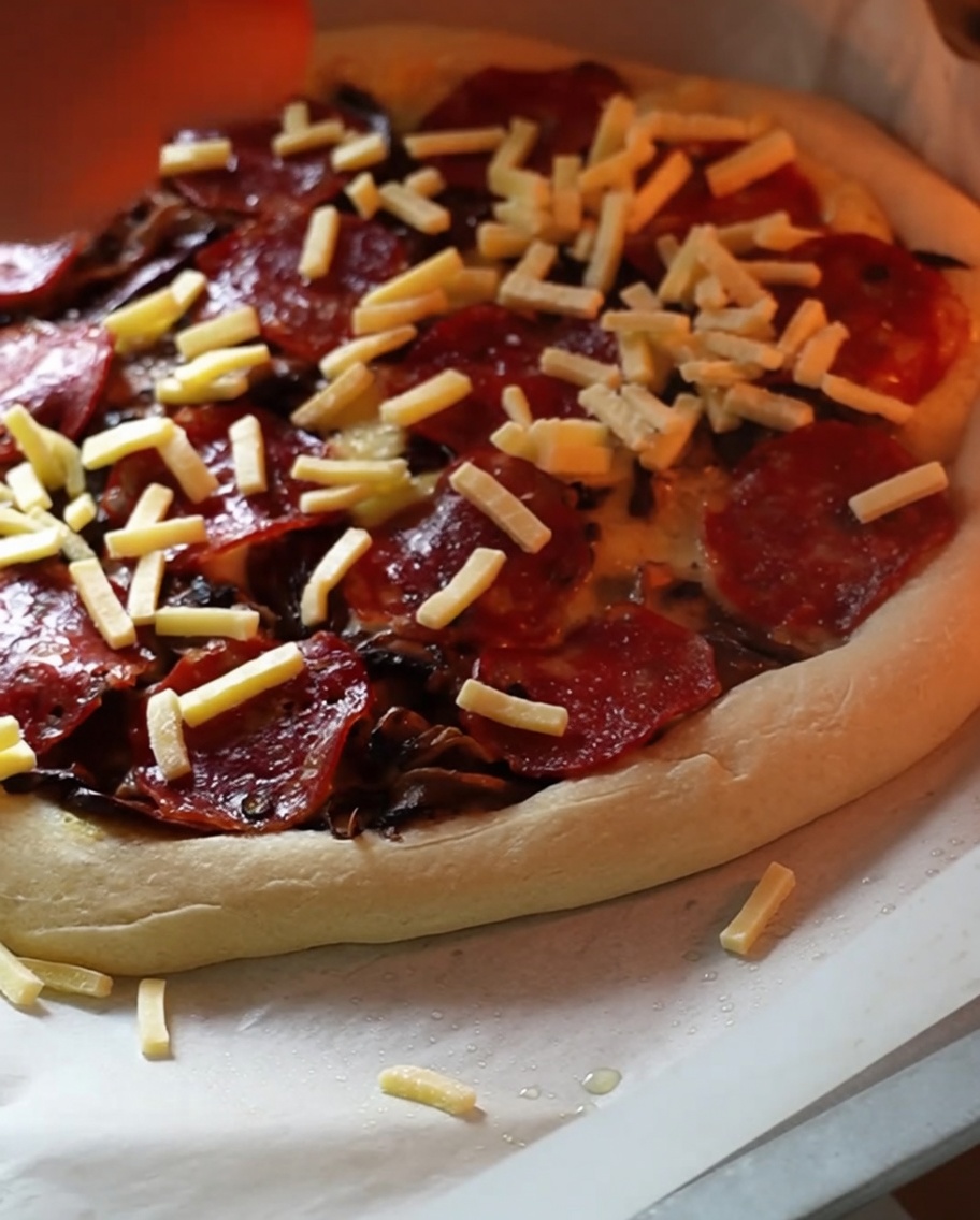 Eine halbfertige Pizza im Ofen bekommt eine zusätzliche Schicht Käse.