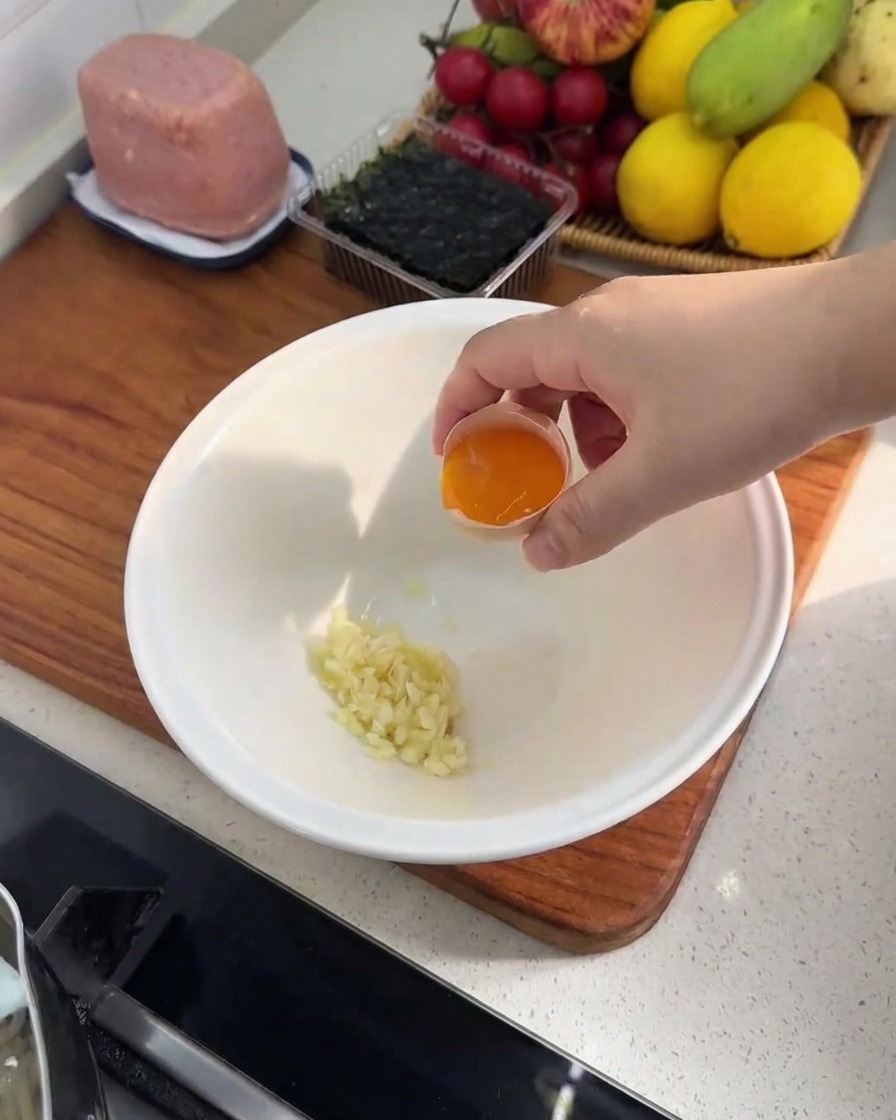 Nahaufnahme einer weißen Schüssel mit gehacktem Knoblauch und einem frischen Eigelb.