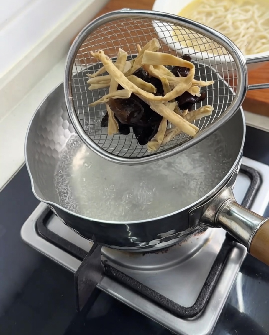 Mu-Err-Pilze und Bambussprossen werden in einem Sieb in einem Topf mit kochendem Wasser blanchiert.