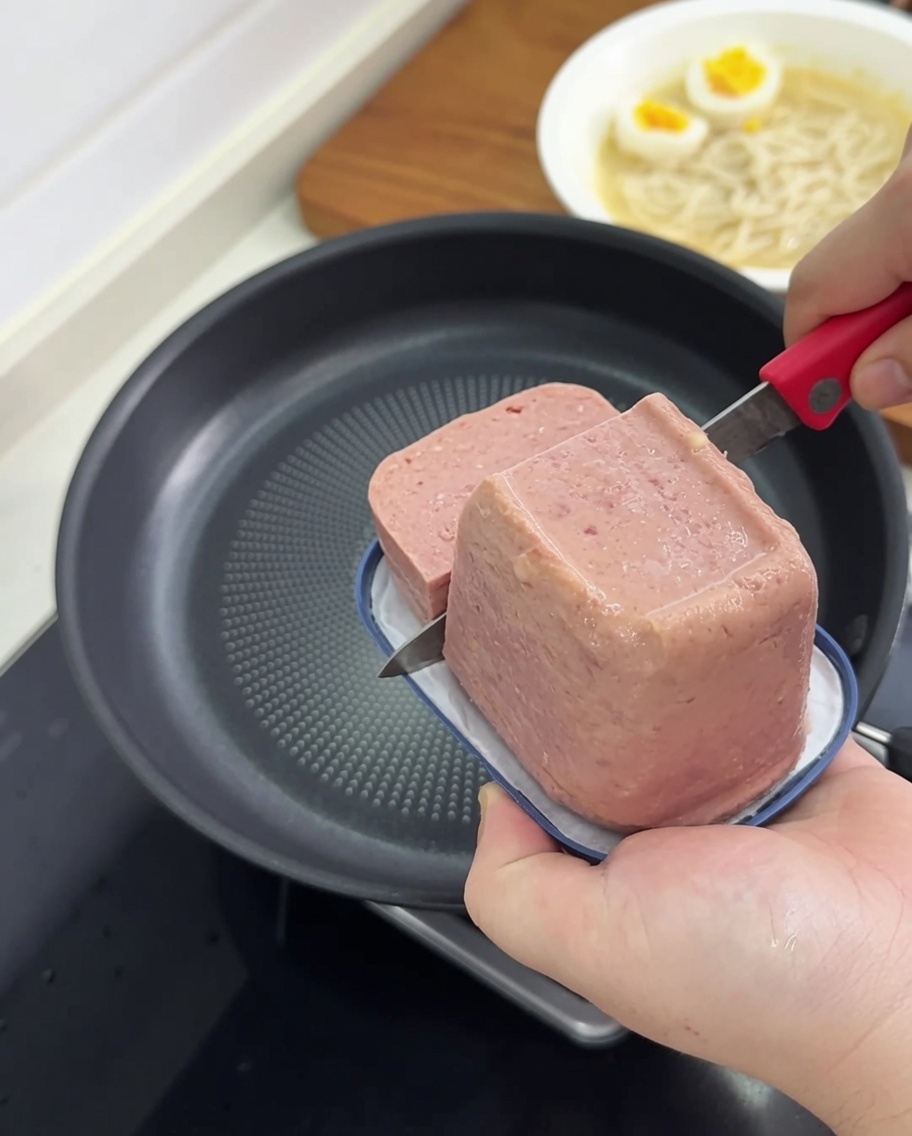 Scheiben von Frühstücksfleisch werden in einer beschichteten Pfanne gebraten, bis sie goldbraun sind.