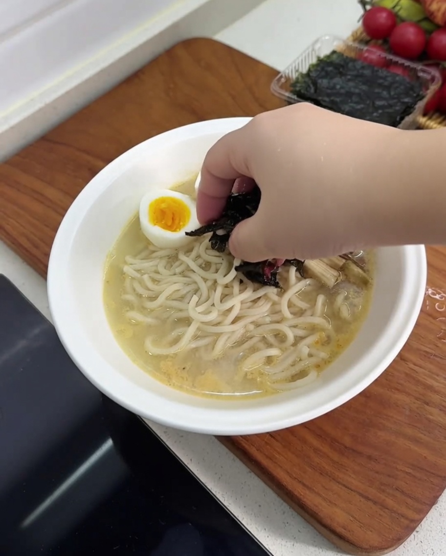 Eine Schüssel Ramen wird mit halbierten hartgekochten Eiern, Pilzen, Bambussprossen und einem Stück Nori-Alge belegt.