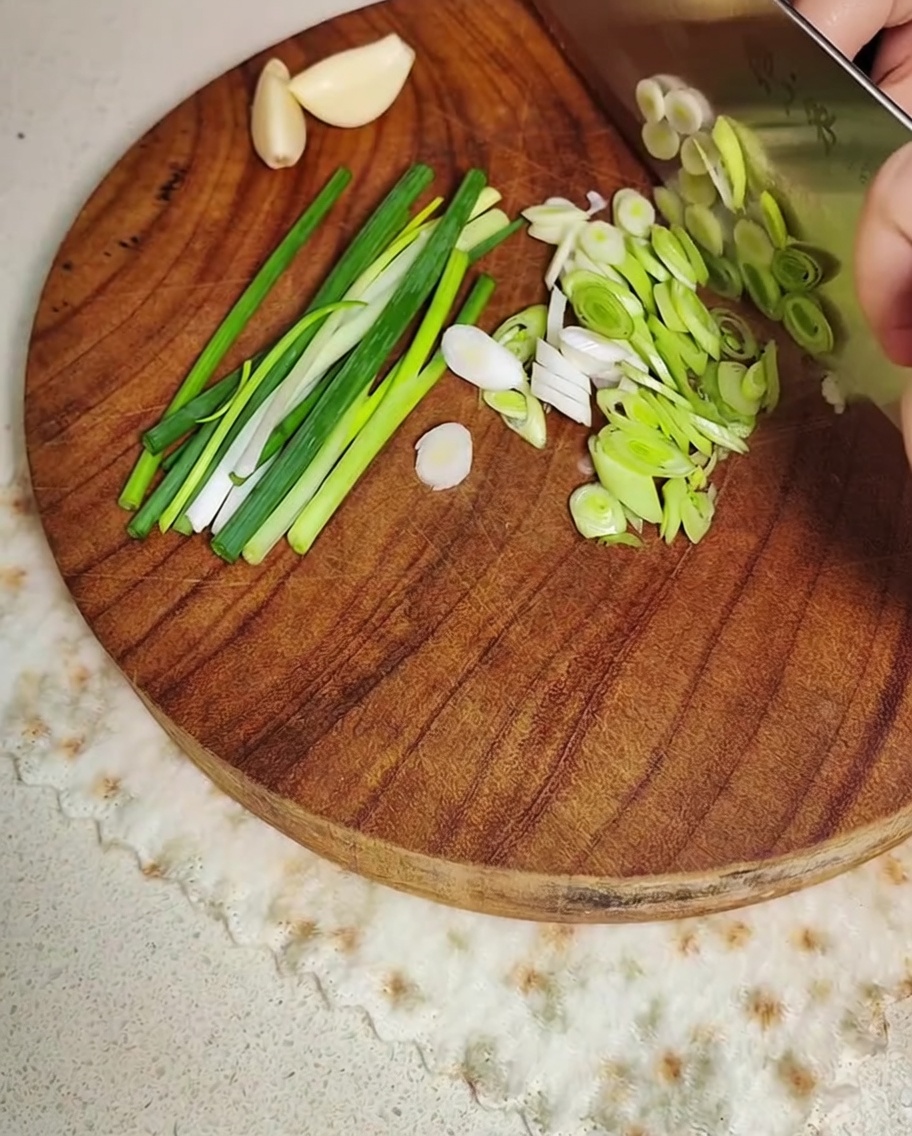 Frühlingszwiebeln und Knoblauch werden auf einem Holzbrett geschnitten.