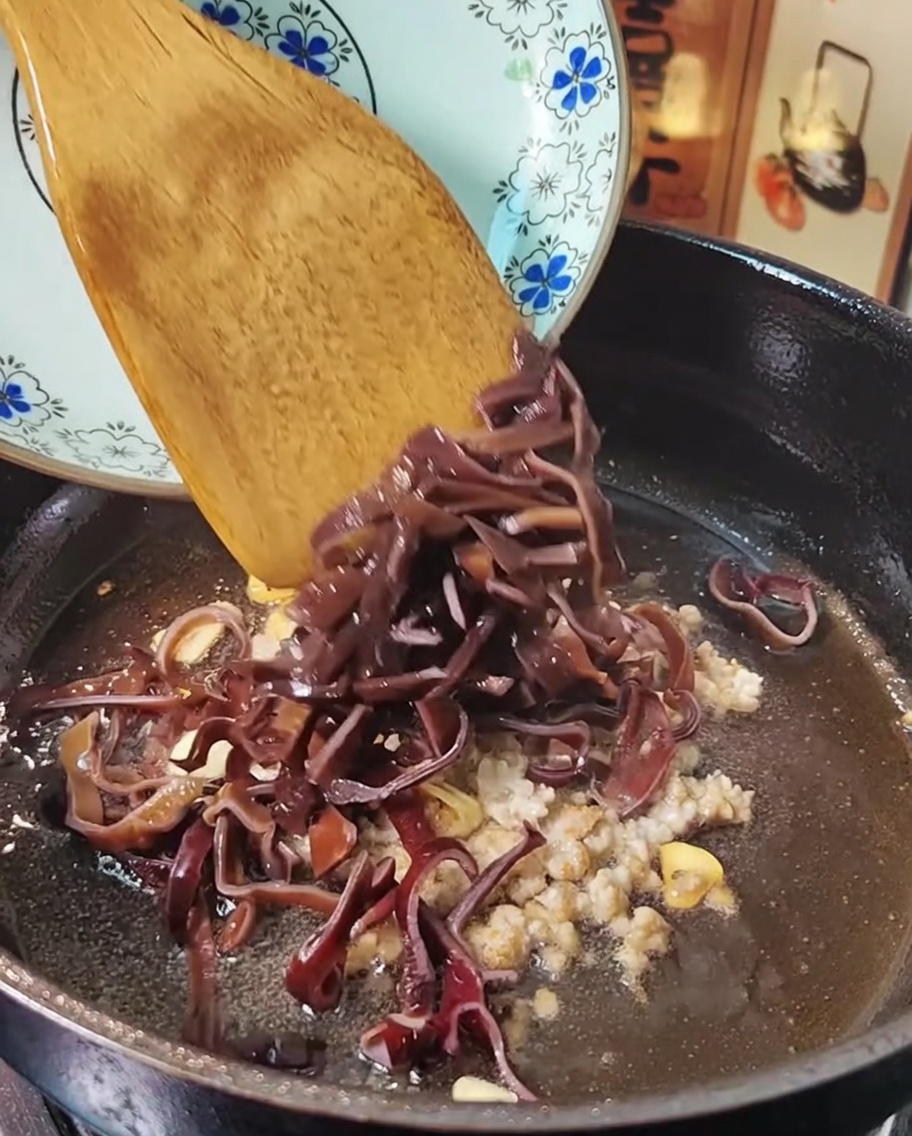 Hackfleisch und Mu-Err-Pilze werden in einer Pfanne mit einem Holzspatel geschwenkt.