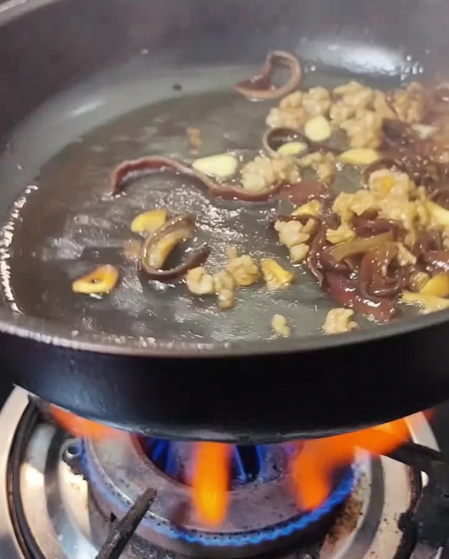 Helle Sojasauce und Austernsauce werden in die Pfanne mit Fleisch und Pilzen gegeben.