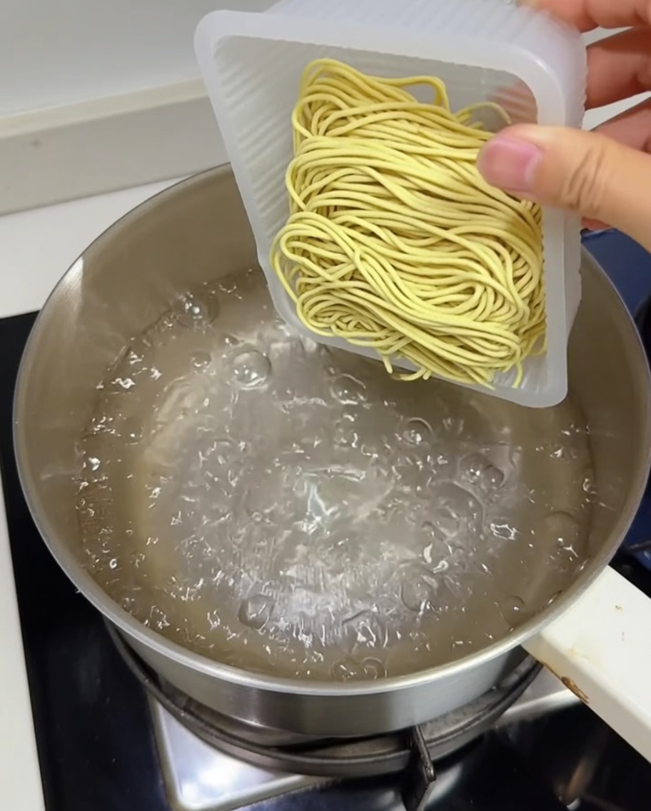 Ein Block frische gelbe Ramen-Nudeln wird in einen Topf mit kochendem Wasser gegeben.