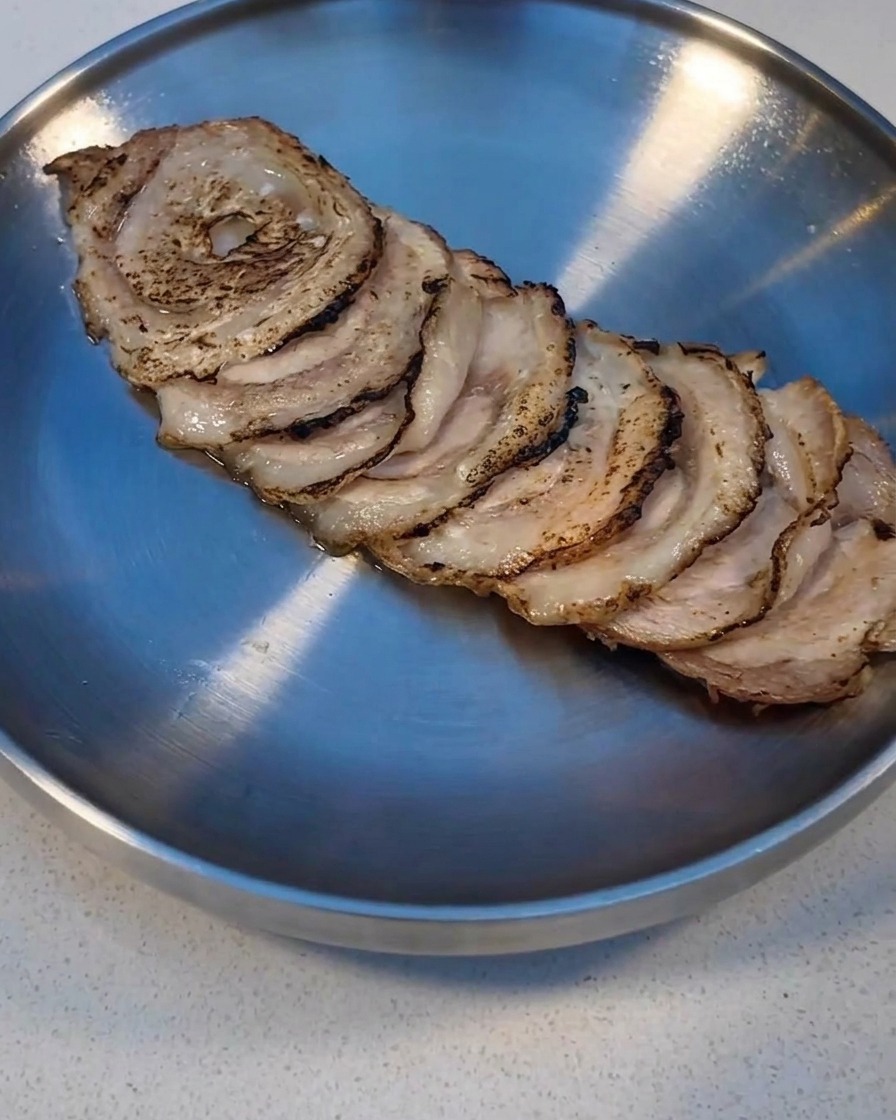 Char Siu-Scheiben werden mit einem Küchenbrenner auf einem Metalltablett angebraten.