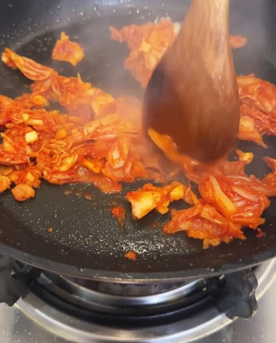 Wasser wird in die Pfanne mit angebratenem Kimchi und Knoblauch gegossen.