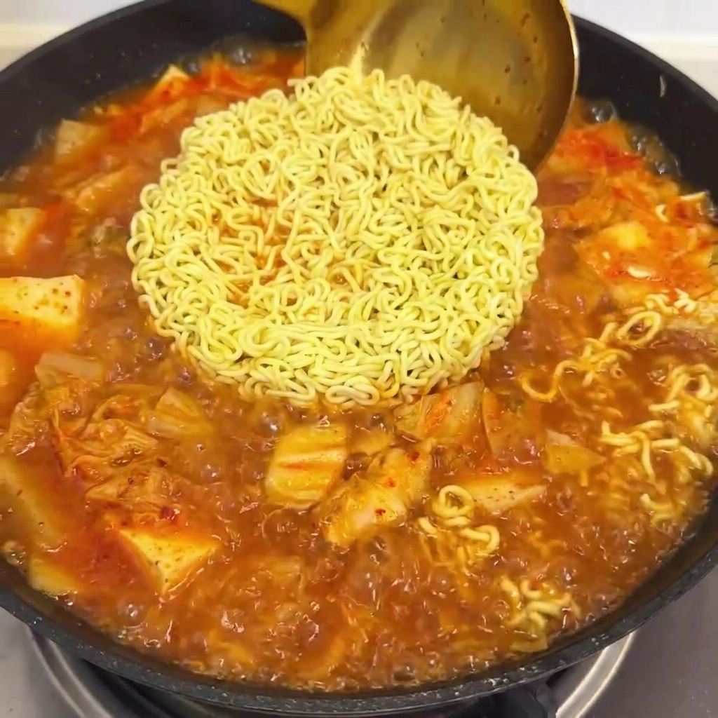 Rote Soße wird in eine Pfanne mit kochenden Ramen-Nudeln und Kimchi-Brühe gegossen.