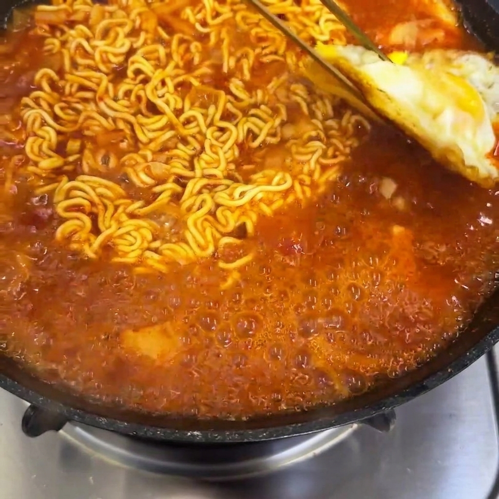 Gebratene Eier werden in eine Pfanne mit köchelnden, würzigen Ramen-Nudeln gelegt.