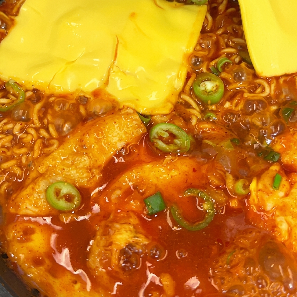 Zwei Scheiben gelber Käse schmelzen auf würzigen Ramen-Nudeln in einer Pfanne.