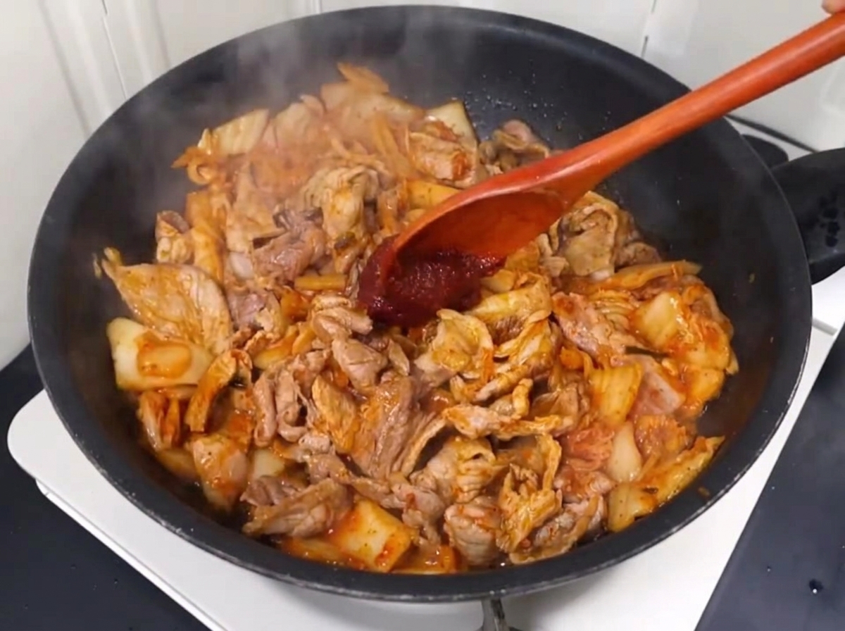 Chilipaste und Chilipulver werden unter das Schweinefleisch-Kimchi-Gemisch gerührt.