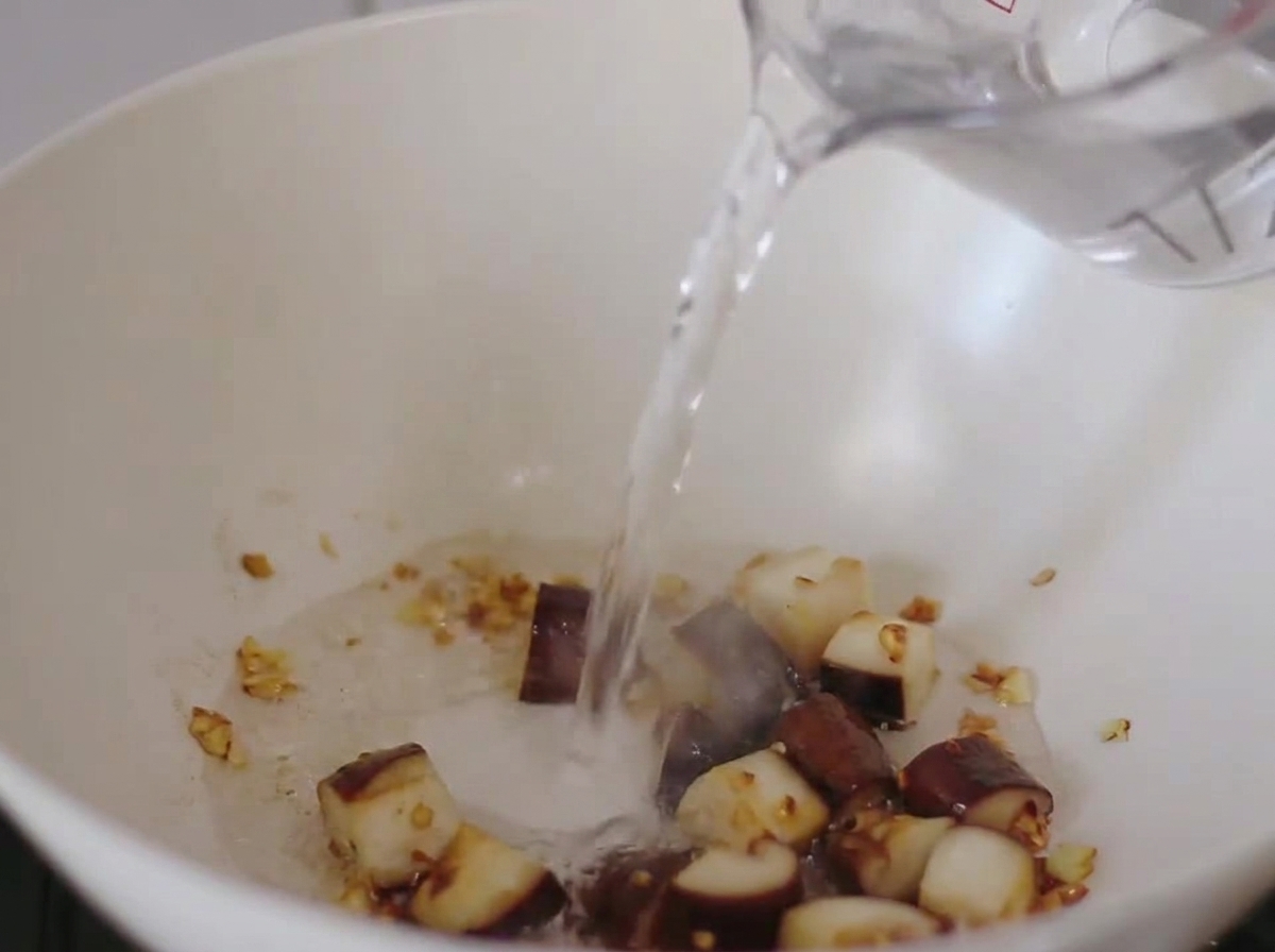Wasser wird in die Pfanne mit den angebratenen Pilzen und Knoblauch gegossen.