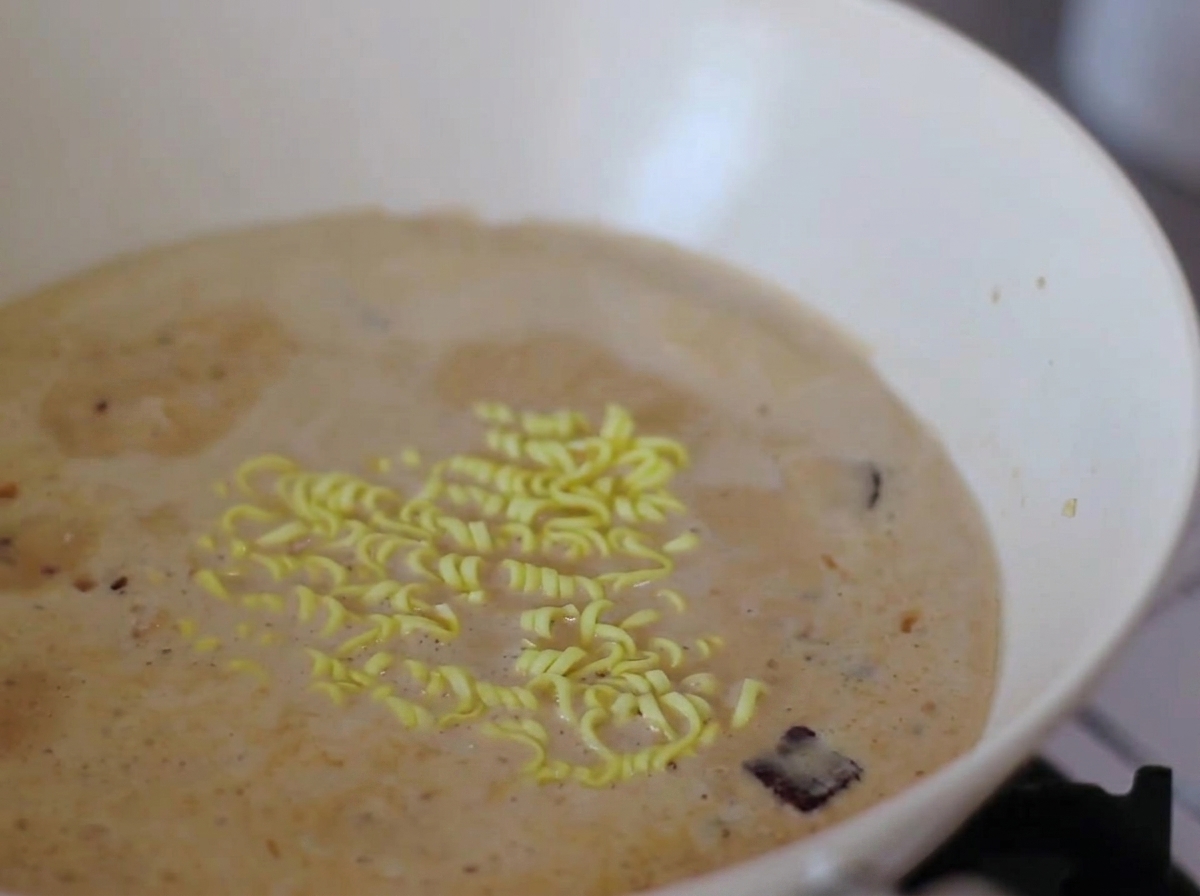 Instant-Nudeln und Narutomaki-Scheiben kochen in der cremigen Brühe.