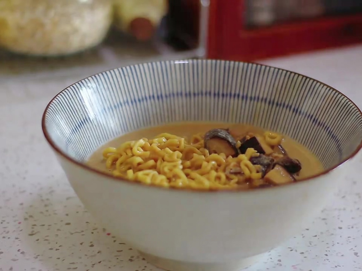 Ramen-Nudeln und cremige Brühe werden in eine gestreifte Servierschüssel geschöpft.
