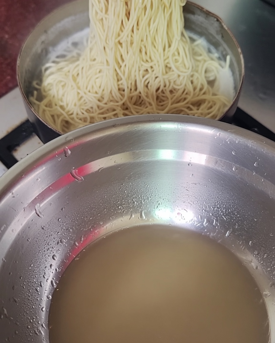Gekochte Nudeln werden mit Stäbchen aus dem Topf gehoben.