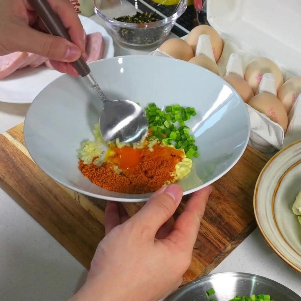 Nahaufnahme eines Löffels, der Eigelb, Knoblauch, Zwiebeln und Gewürze in einer weißen Schüssel zu einer glatten, dicken Paste vermischt.