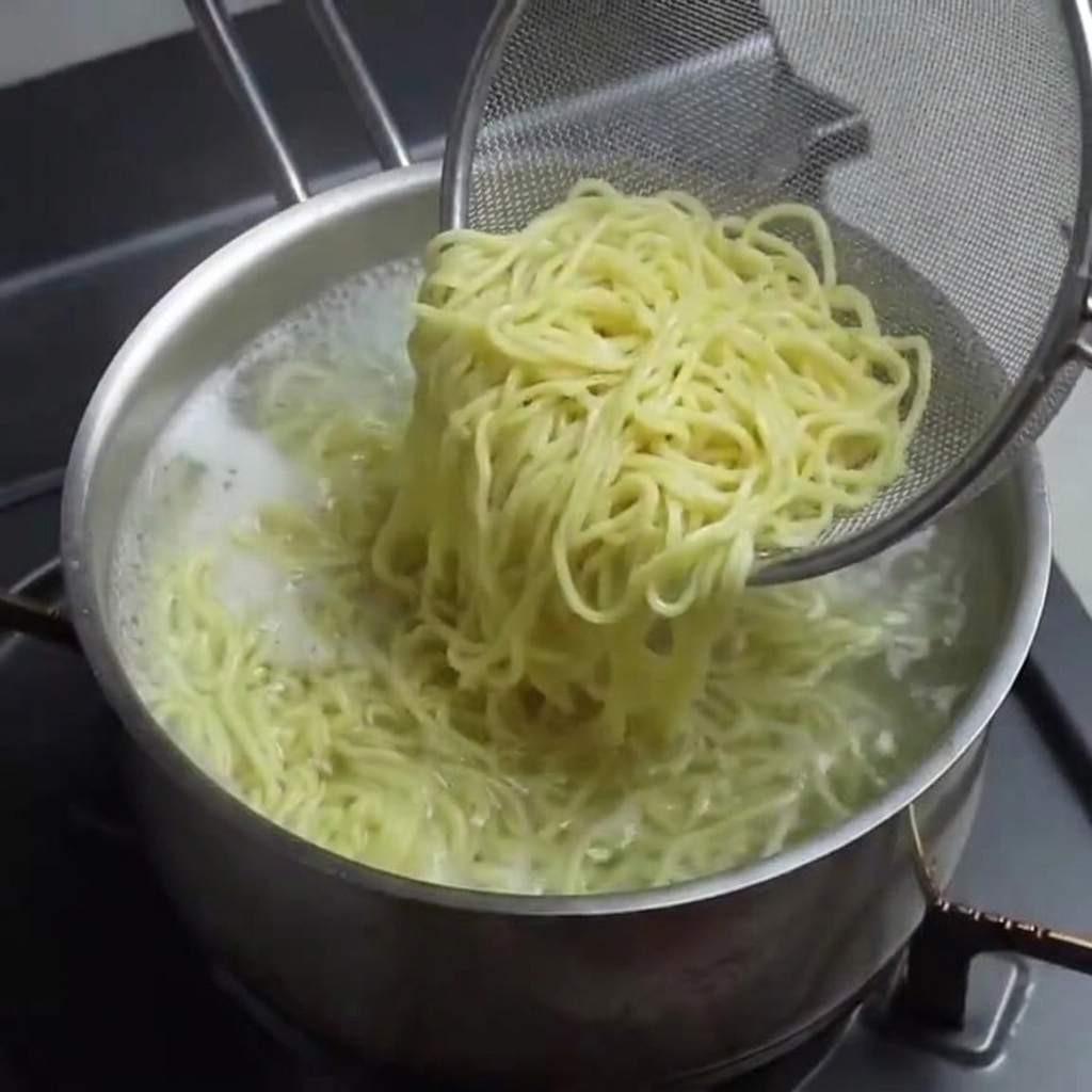 Gekochte Ramen-Nudeln werden mit einem Sieb aus dem Topf gehoben.