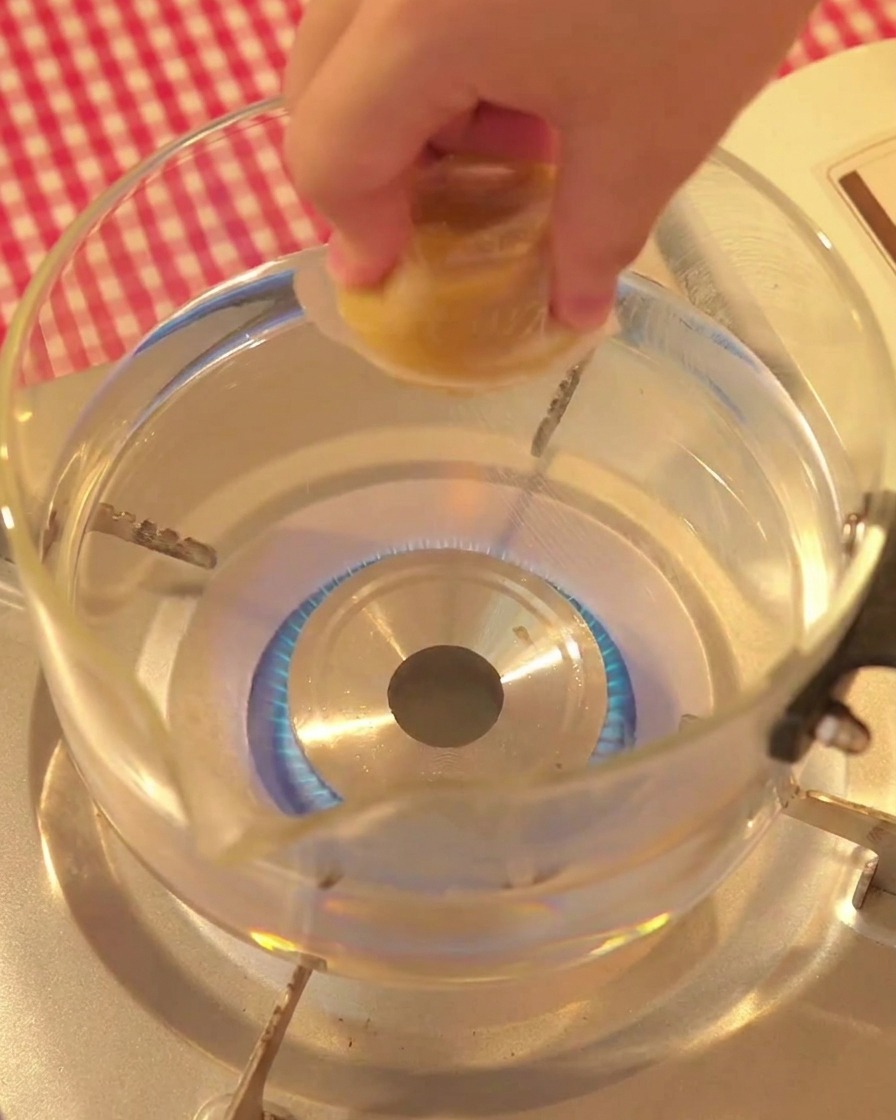 Eine Hand gibt einen Brühwürfel in einen Glastopf mit kochendem Wasser.