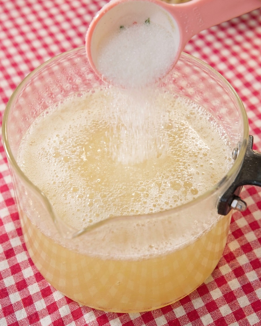 Ein Löffel weißer Zucker wird in die köchelnde Ramen-Brühe gegeben.