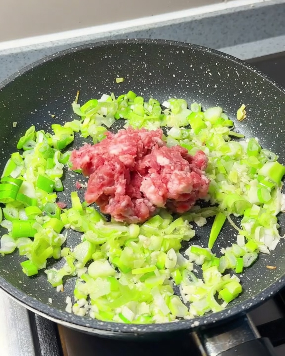 Ein Häufchen rohes Hackfleisch in der Mitte einer Pfanne mit angebratenen Frühlingszwiebeln und Knoblauch.
