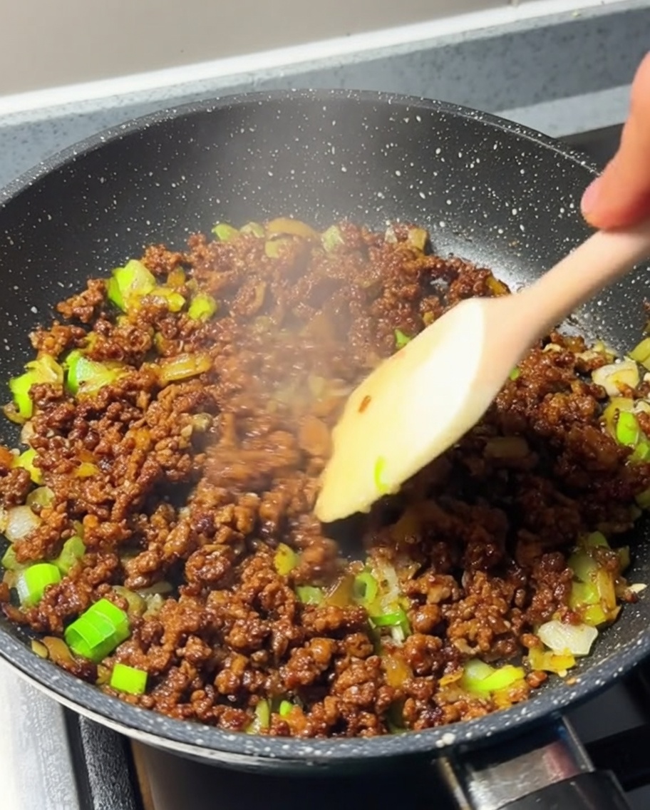Hackfleisch wird in einer Pfanne aktiv umgerührt und ist nun vollständig gebräunt.