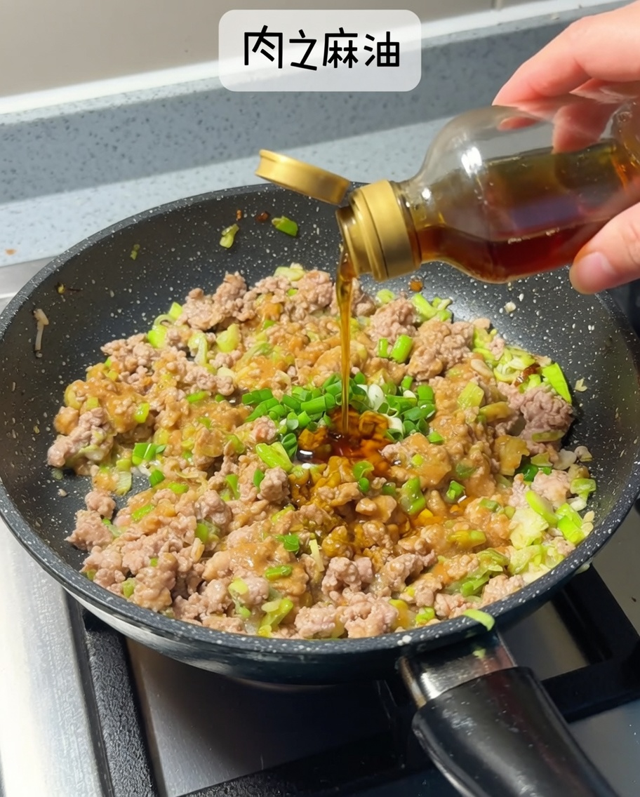Dunkelgoldenes Sesamöl wird aus einer kleinen Glasflasche in die Pfanne mit der Fleisch-Miso-Mischung geträufelt.