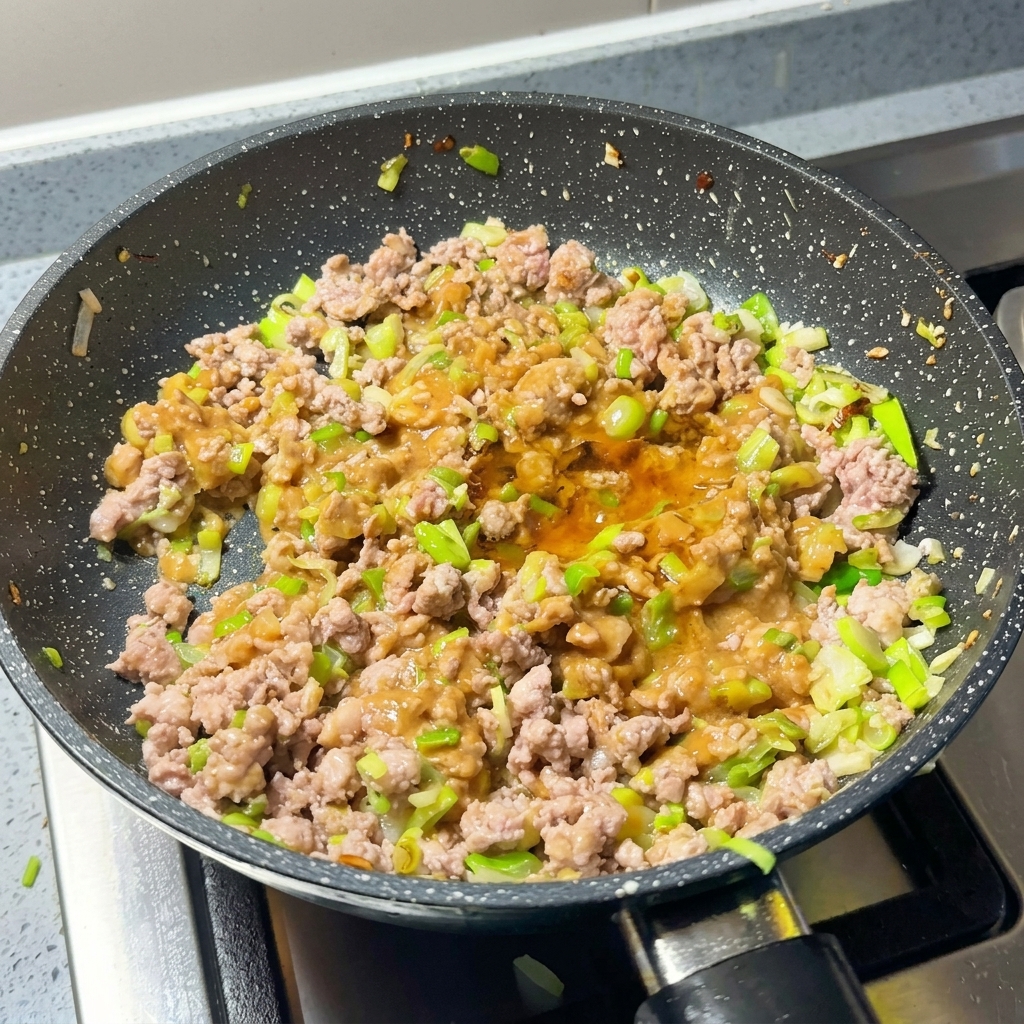 Eine Pfanne mit gebratenem Hackfleisch und Miso wird mit Chilipulver und Zucker gewürzt.