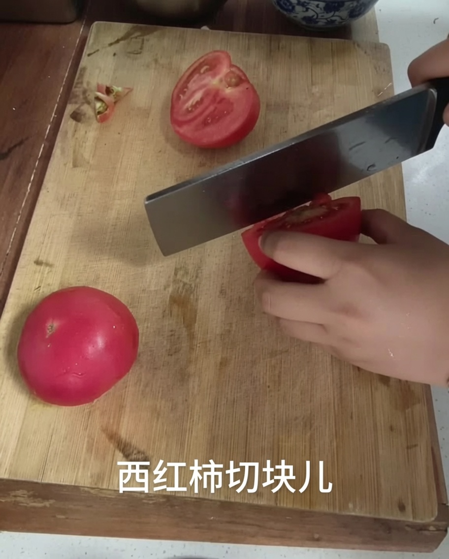Ein Küchenmesser schneidet eine Tomate auf einem Holzbrett in Stücke.