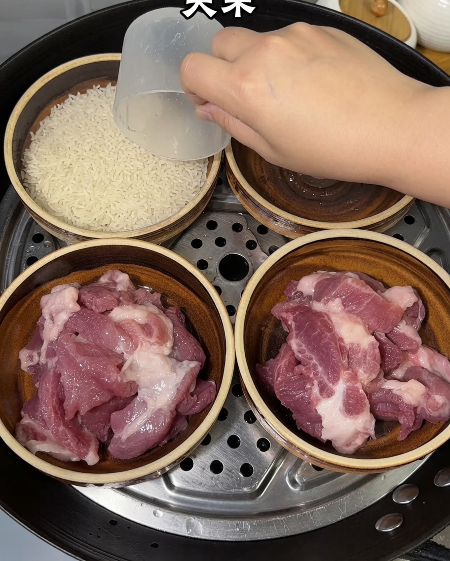 Eine Hand gibt mit einem Messbecher rohen Reis in die Schüsseln mit Schweinefleisch.
