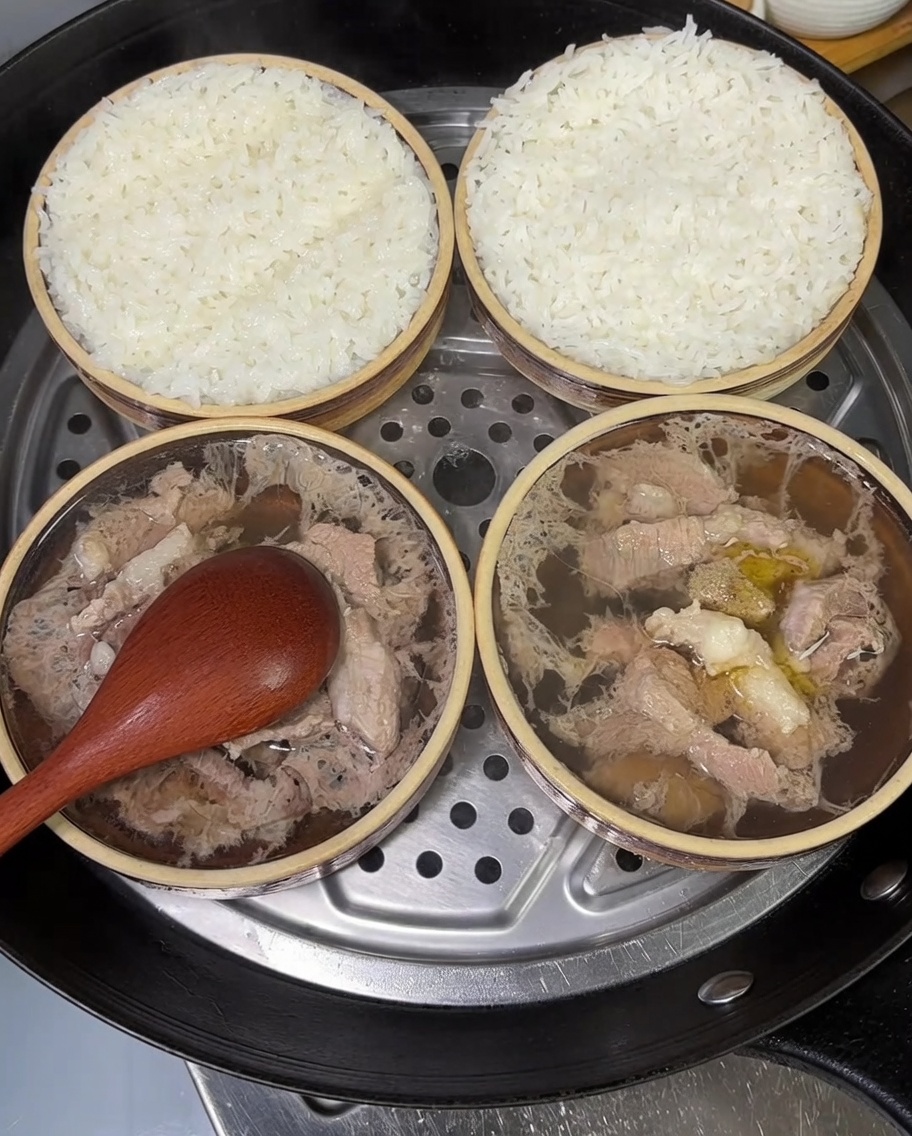 Zwei kleine Schüsseln mit gedämpftem Schweinefleisch und Reis, garniert mit frischen, gehackten Frühlingszwiebeln.