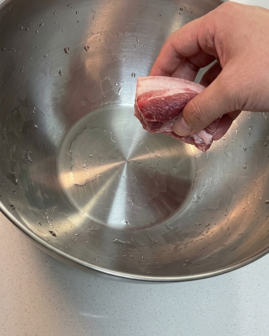 Schweinebauch und Schweineschulterknochen weichen in einer großen Schüssel mit kaltem Wasser ein.
