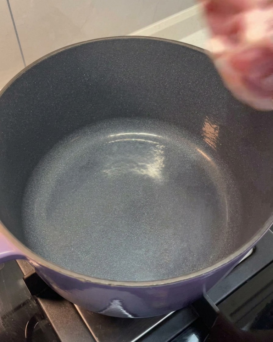 Das abgespülte Fleisch und die Knochen werden in einen großen lilafarbenen Topf gegeben.