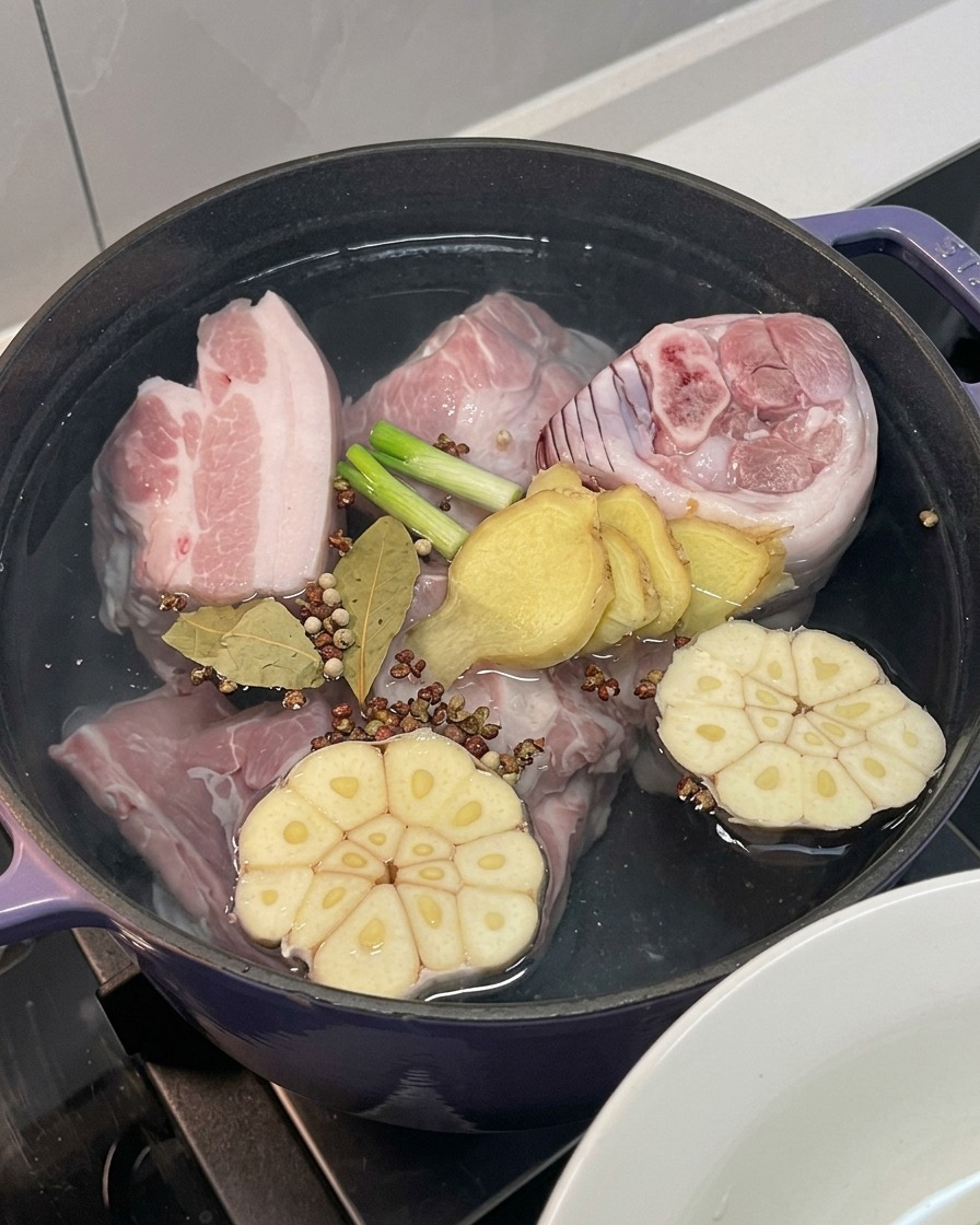Schweinefleisch im Topf mit Zwiebel, Knoblauch, Ingwer, Frühlingszwiebeln und ganzen Gewürzen.
