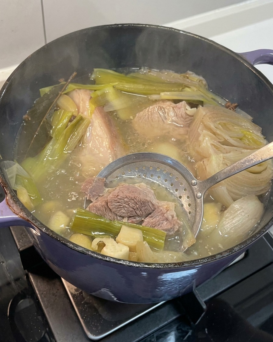 Entfernen von weich gekochten Zwiebel-, Knoblauch- und Ingwerstücken aus der fertigen Brühe.