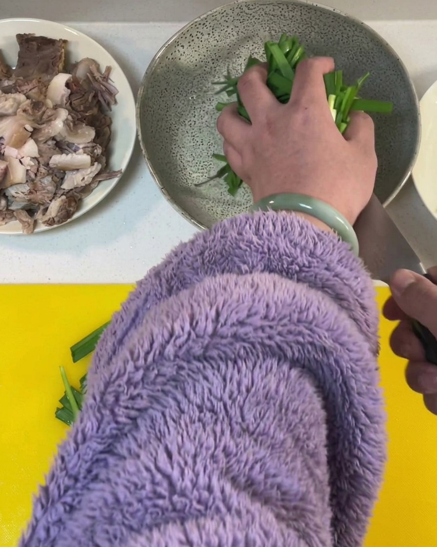 Frischer grüner Schnittlauch wird auf einem gelben Schneidebrett in Stücke geschnitten.