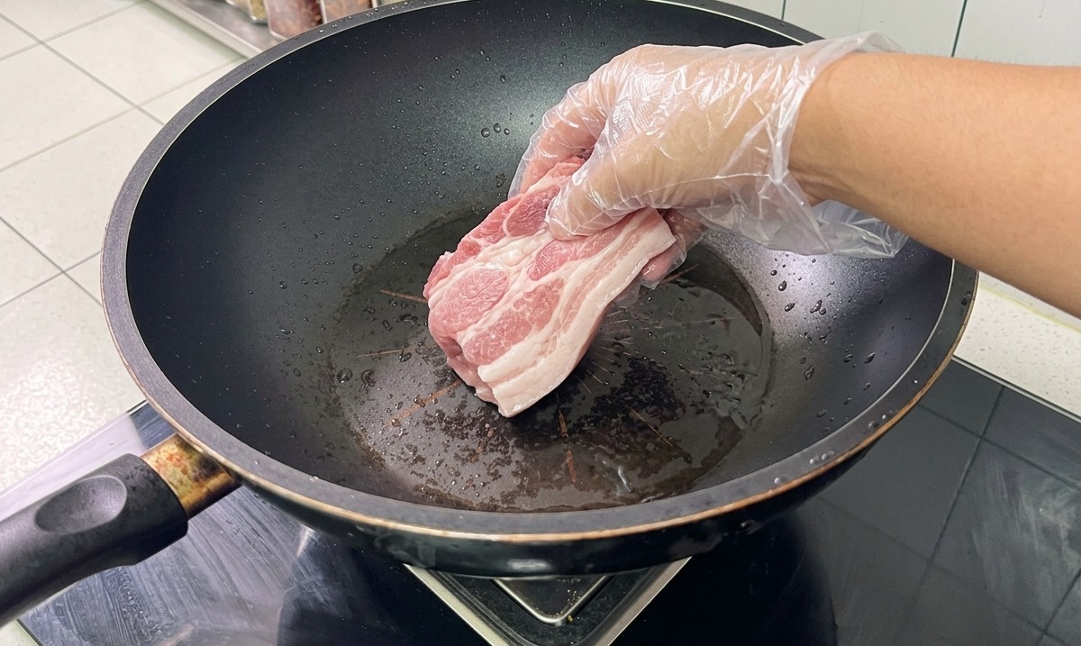Schweineknochen und Schweinebauch werden in einem Wok mit Wasser und Gewürzen blanchiert.