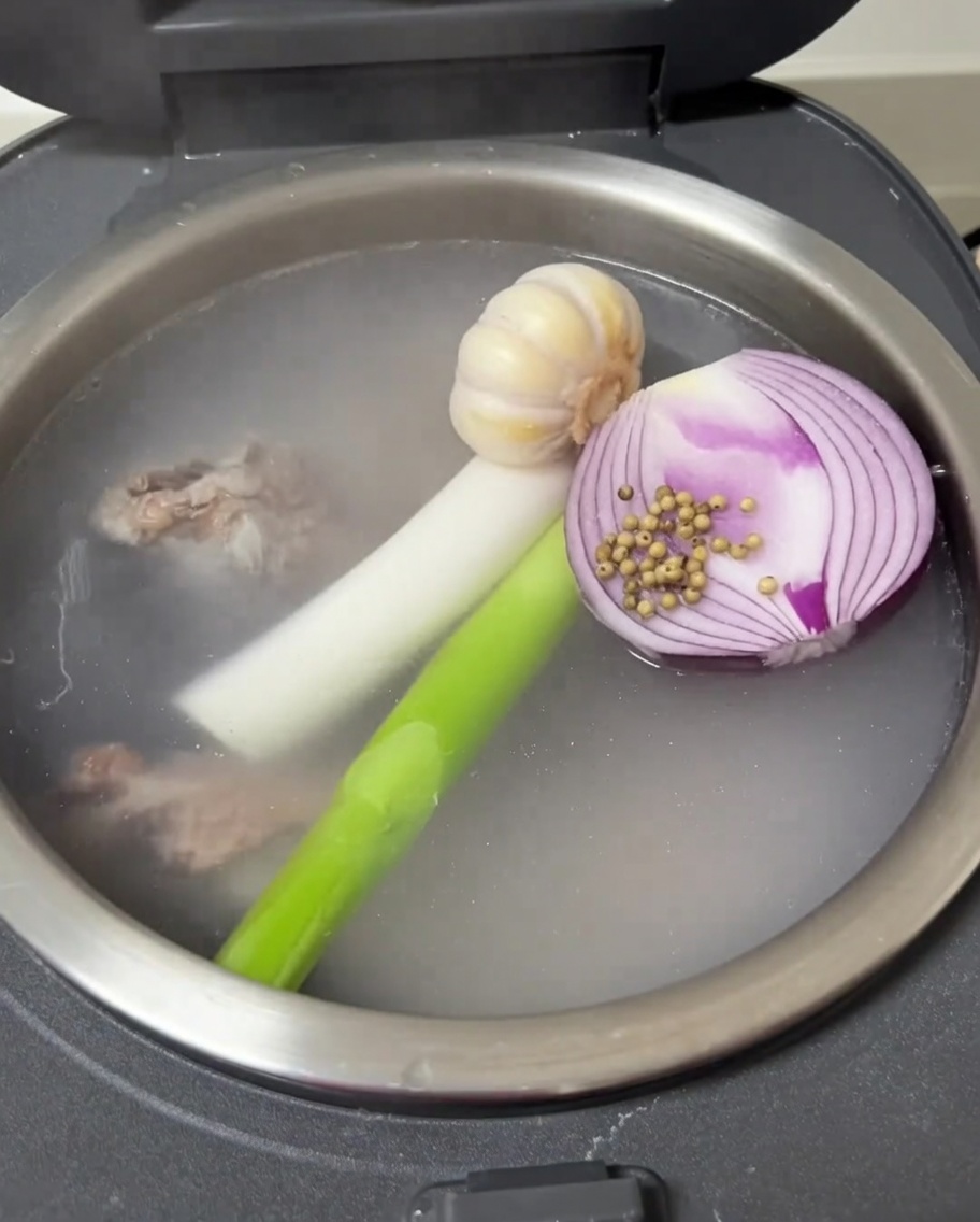 Knoblauch, Zwiebel, Frühlingszwiebeln und weißer Pfeffer schwimmen mit den Rippchen im Reiskocher.