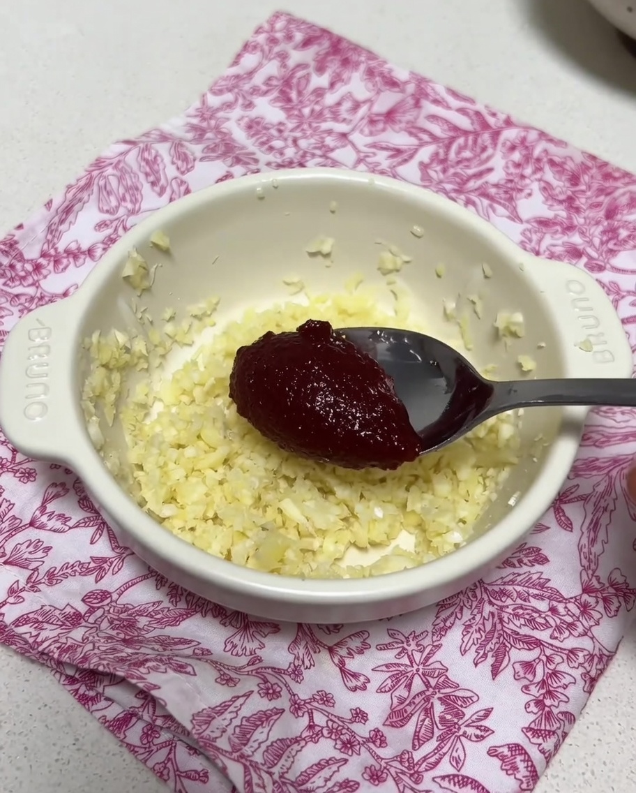Eine kleine Schüssel mit gehacktem Knoblauch und koreanischer Chilipaste, die mit etwas Brühe verrührt werden.