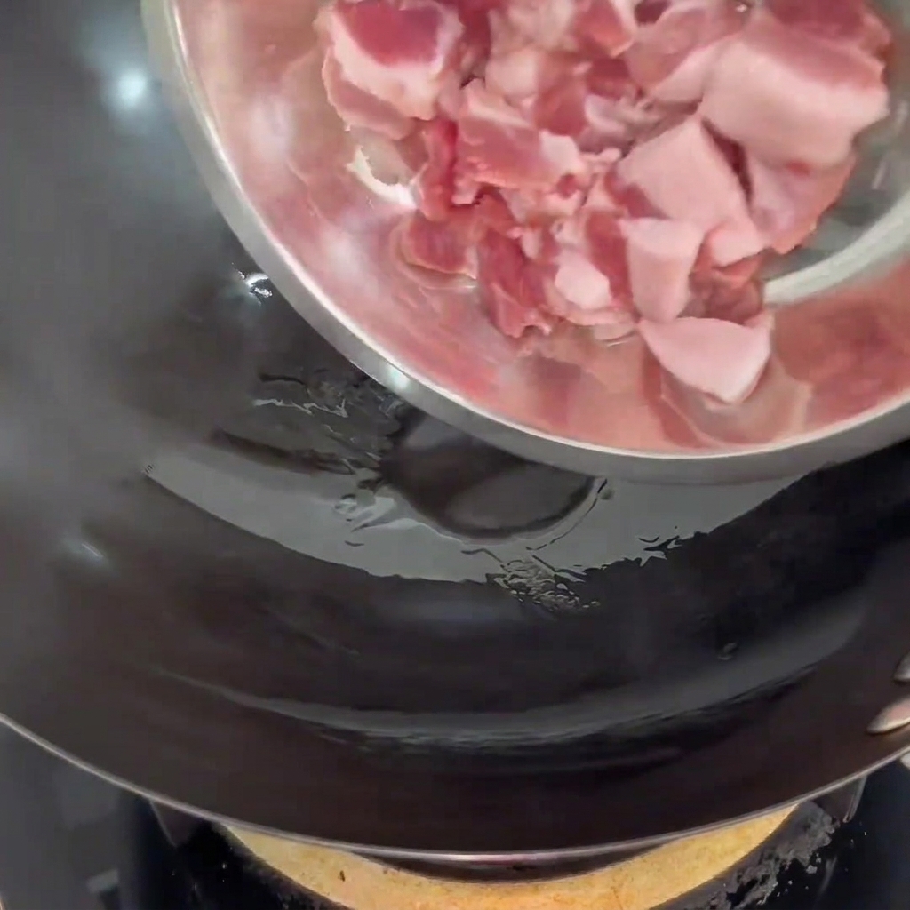 Schweinebauchscheiben werden in einen heißen Wok mit etwas Speiseöl gegeben.