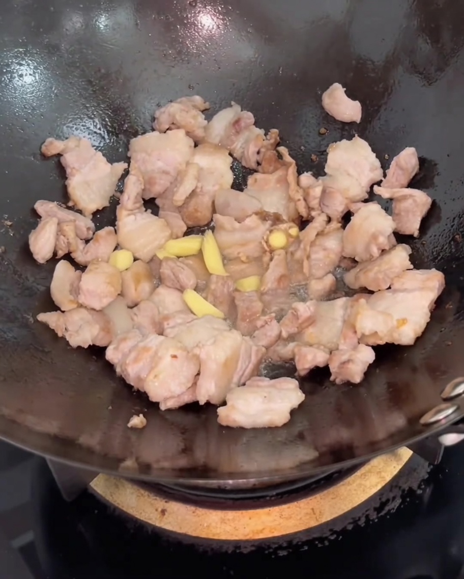 Ingwerscheiben werden zum Schweinebauch in den Wok gegeben und untergerührt.