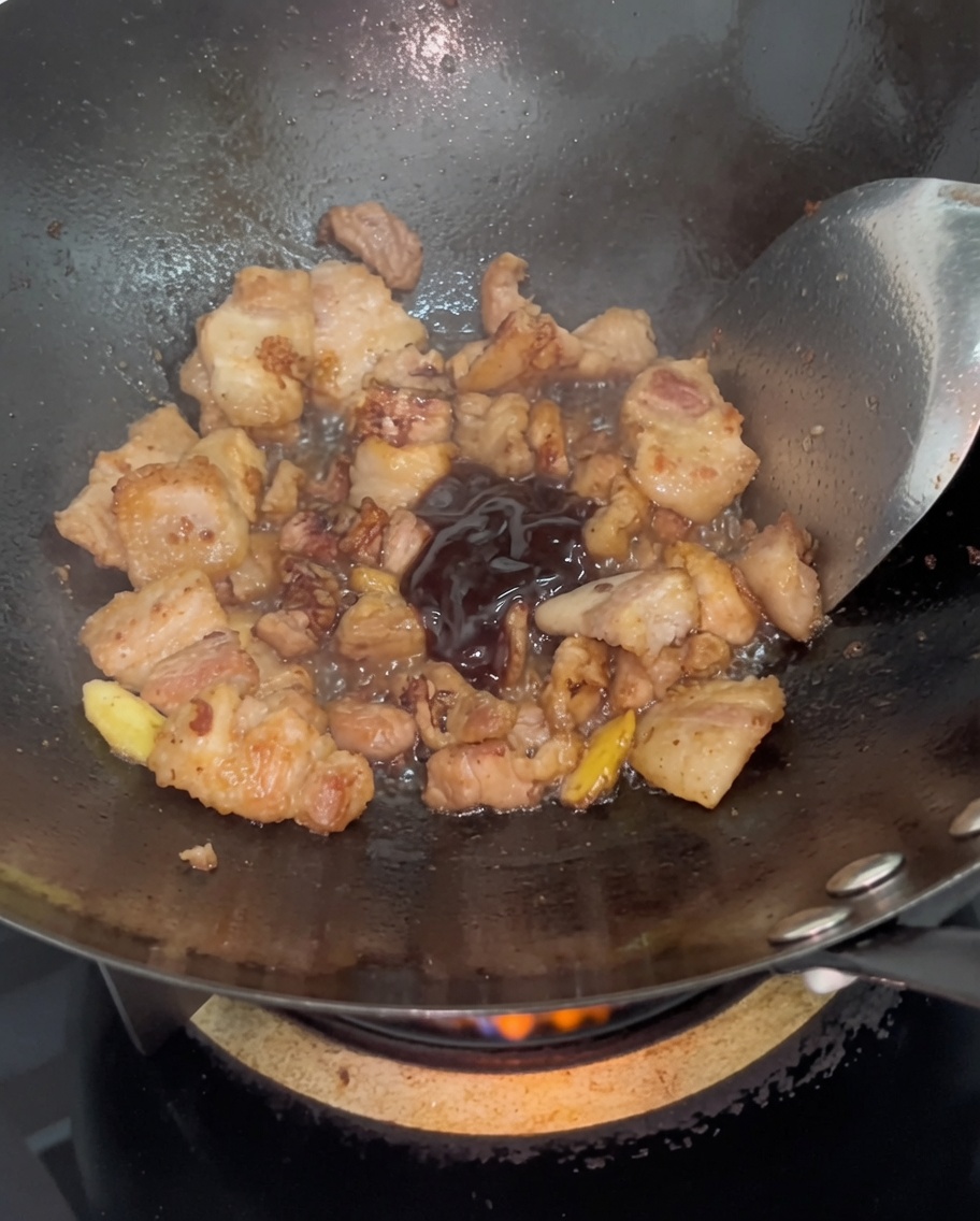 Dunkle Austernsauce wird in gebräunte Schweinebauchscheiben in einem heißen Wok eingerührt.