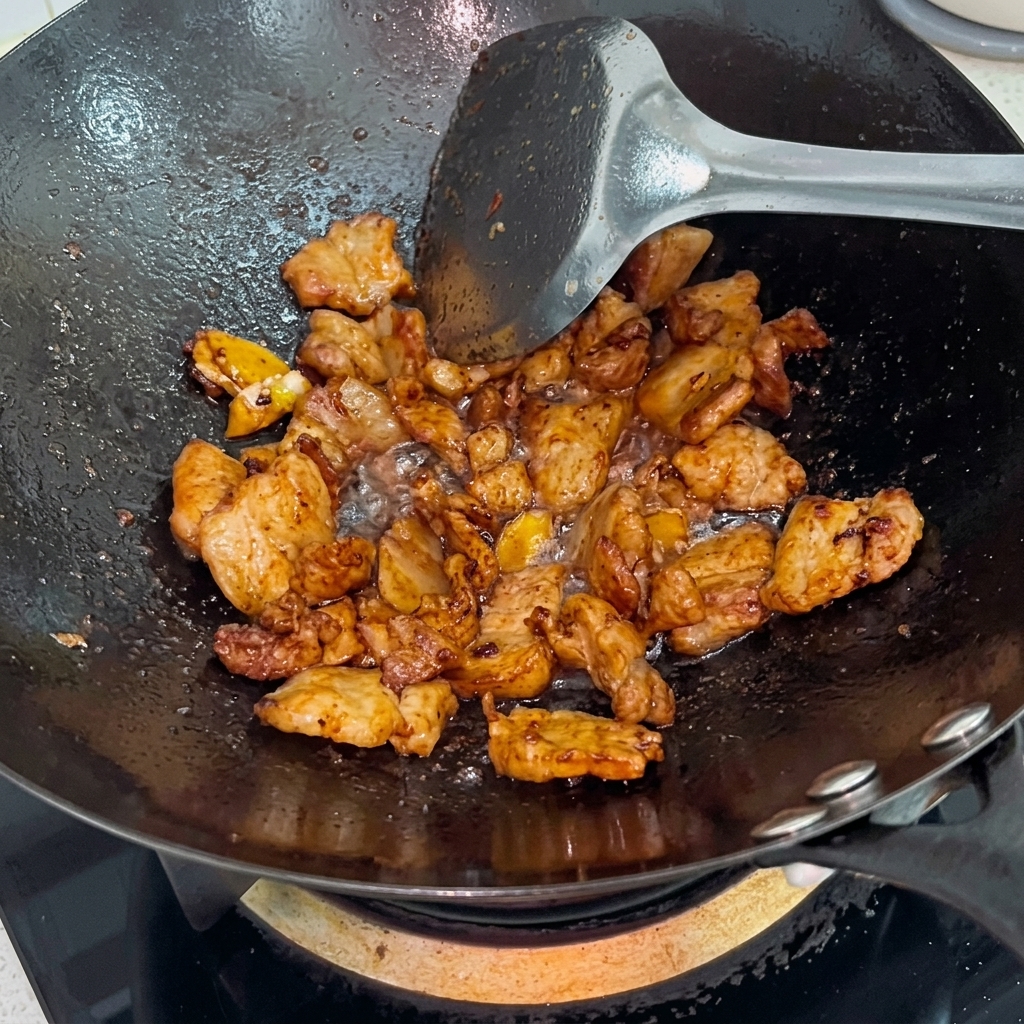 Weißer Zucker wird über glänzenden, gebräunten Schweinebauch im Wok gestreut.
