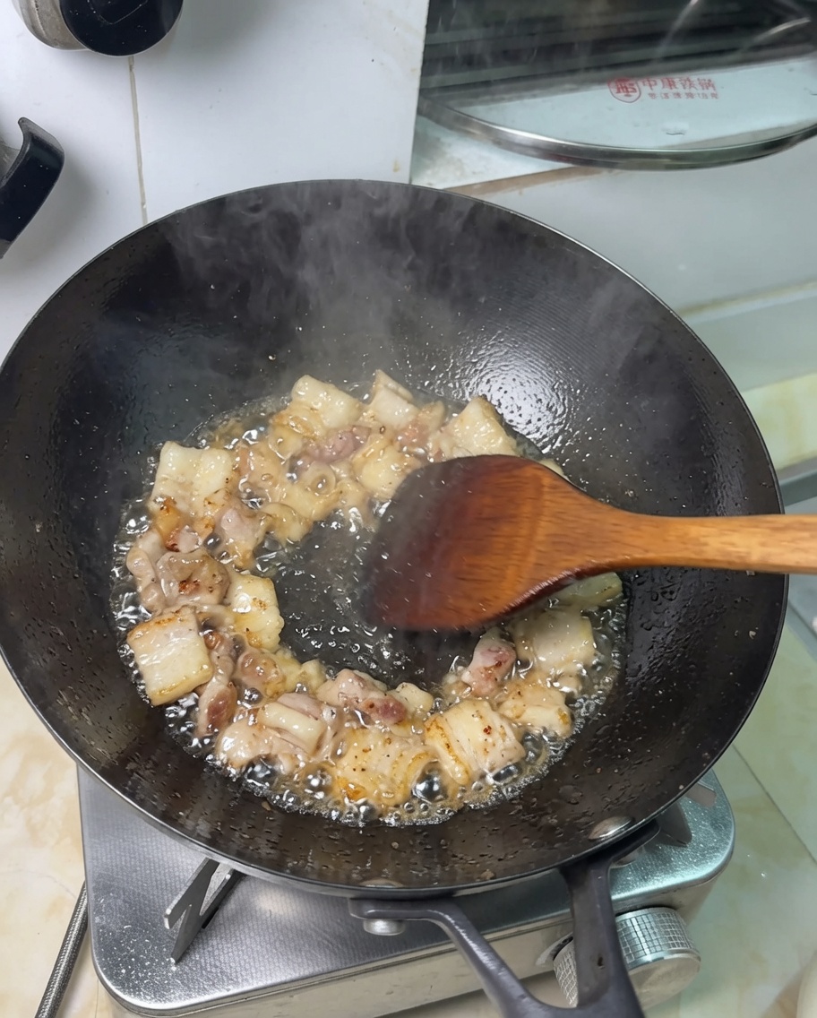 Schweinebauchstücke, die in ausgelassenem Fett im Wok braten.