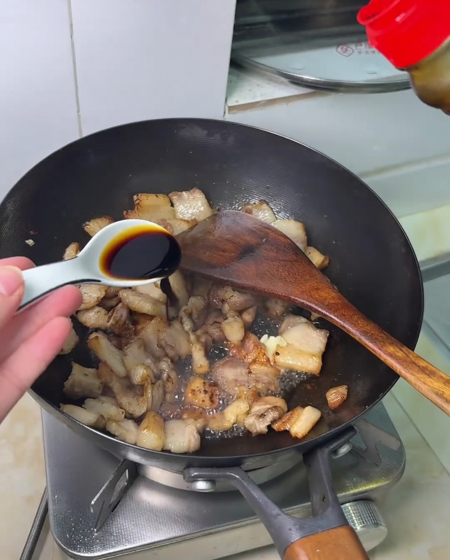 Sojasauce wird über den angebratenen Schweinebauch in einem Wok geträufelt.